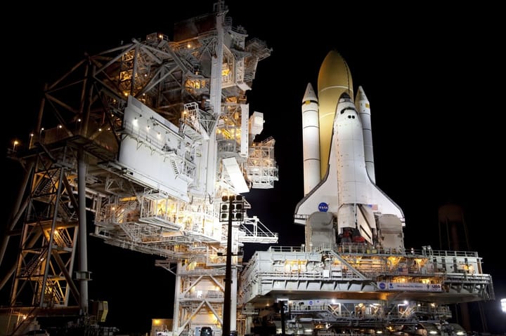 A space shuttle on a launch pad surrounded by supportive infrastructure, seen at night.